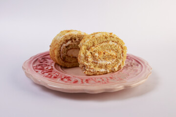 two slices of cream-filled sponge cake roll elegantly arranged on a pink decorative ceramic plate with a subtle floral pattern. Soft directional lighting accentuates the delicate spiral swirls of gol © nicholasgeorgiou