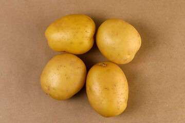 A high-resolution studio photograph of a cluster of four small yellow potatoes arranged closely on a neutral beige surface, showcasing the tubers’ matte skin texture, gentle color variations,