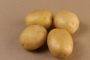 A high-resolution studio photograph of a cluster of four small yellow potatoes arranged closely on a neutral beige surface, showcasing the tubers’ matte skin texture, gentle color variations,