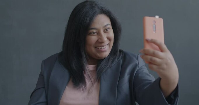 Slow motion portrait of pretty young lady taking selfie posing for smartphone camera on black background. Photography and modern technology concept.