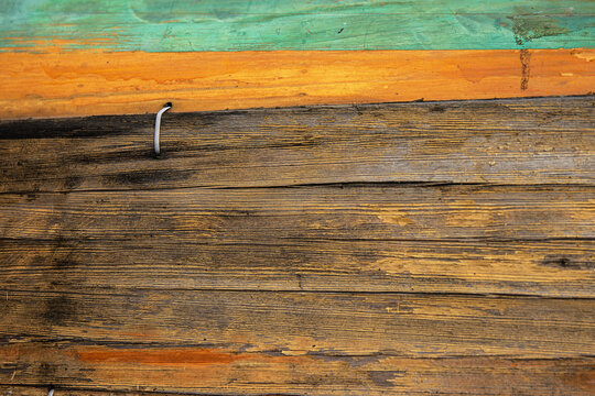 A closeup of the aged weathered wooden side of a boat with worn textures and painted green, yellow and orange trim. 
