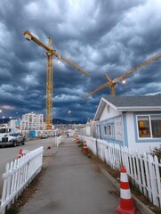 Construction site with cranes under dark stormy clouds and overcast sky during early evening