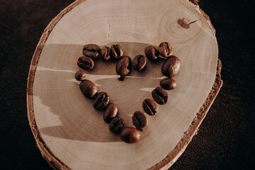 Heart shape arranged from coffee beans on a natural wooden slice in warm lighting