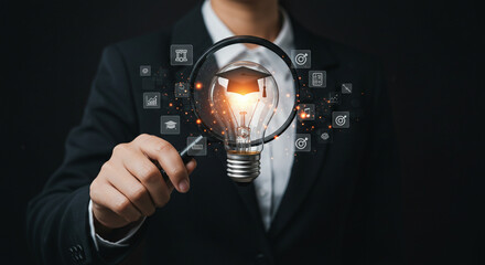 A person holding a magnifying glass over a lightbulb with a graduation cap inside and icons around it