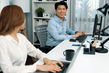 Obraz premium Smiling Asian man talking with woman colleague in planning marketing report project on laptop casual day while searching database on working desk at modern home office at side view image. Infobahn.