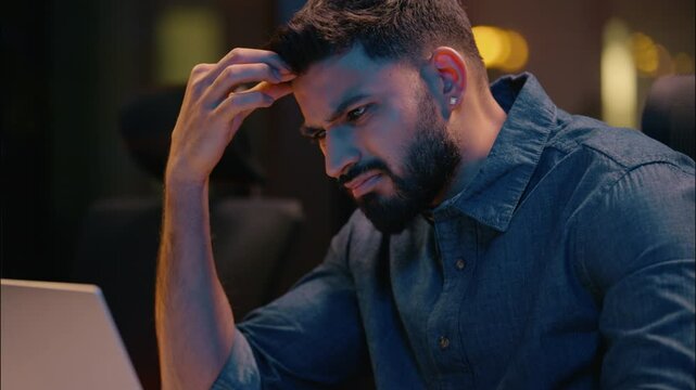 Tired stressed Indian man businessman business employer working laptop overtime evening night office exhausted upset frustrated male worker programmer guy stress headache difficult problem overwork
