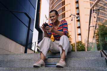Frustrated young woman sits on stairs, squinting at smartphone screen with distressed expression,...