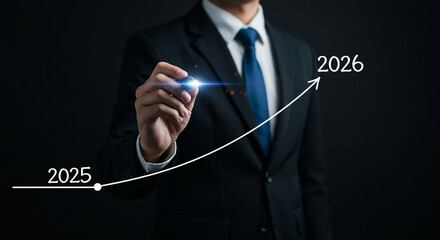 A businessman in a suit drawing an upward trending graph from year 2025 to 2026 on a dark background