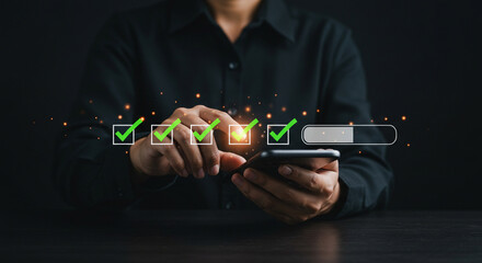 Person using a smartphone with check marks and a loading bar displayed on the screen in a dark setting