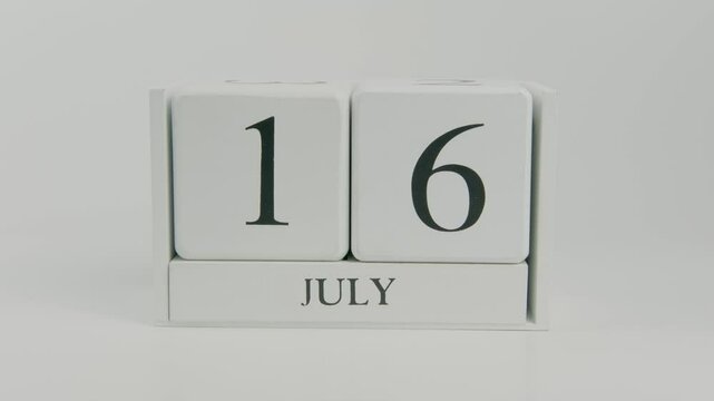 A hand flips a wooden calendar from July 16th to July 17th on a white background, indicating the shift of time