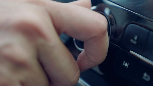 Male hand adjusts tuning of car radio. Driver turns up volume. Passenger searches for their favorite radio station on digital radio in car. Close-up. Listen to music and travel in your car