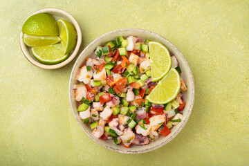 Fresh and vibrant peruvian seafood ceviche with shrimps, octopus, tomatoes, cucumber and parsley, served with lime in a bowl on a light green background from above, dish of Peru
