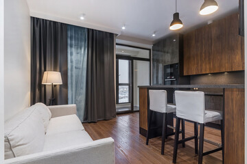Elegant kitchen interior design. Grey furniture decorated with dark wood panels. White .sofa, small balcony.