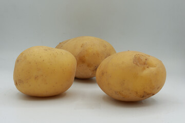 Clean composition featuring three whole yellow potatoes on a seamless white surface. The organic shape and earthy tones highlight their natural simplicity, ideal for food-related content such as healt