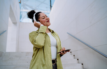 Cheerful woman with wireless headphones enjoys music and browses her smartphone. Female immerses in...