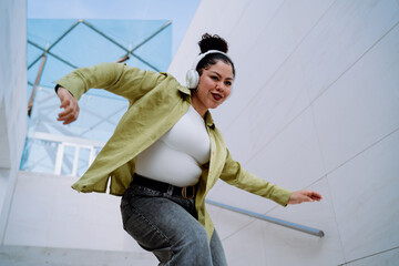 Cheerful young woman moves with enthusiasm, wearing wireless headphones and embracing the music....