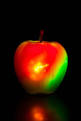 Glowing apple with vibrant light reflection on dark background, fresh and artistic.