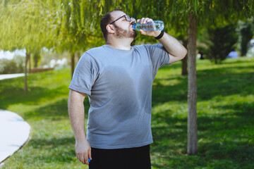 A man with overweight drinking water after jogging in a public park.