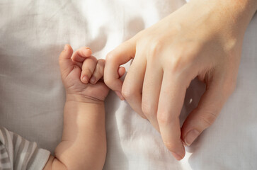 Mother Baby Connection. Newborn child holding his mom's hand while they lying in bed, touching...