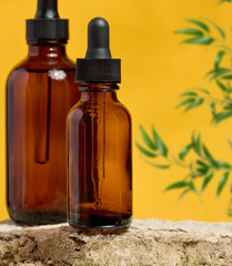 Amber glass dropper bottles on a natural stone surface with a yellow background and green plant elements.