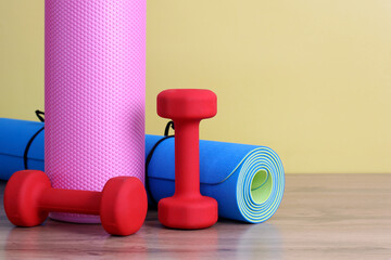two red dumbbells, a yoga mat and a pink MFR massage roller on a yellow background. an empty space for your text on the right.