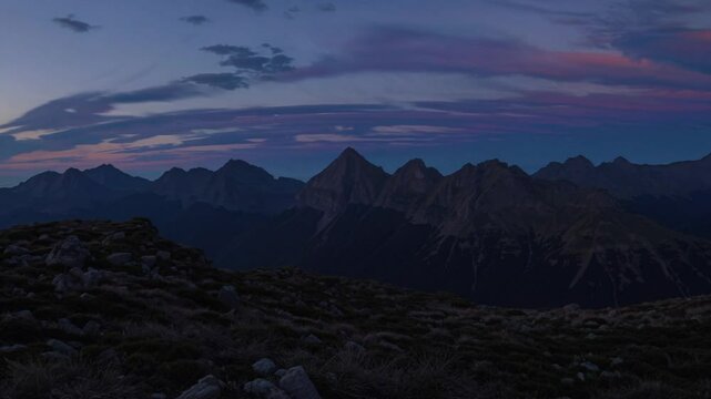 Warm golden light transforming mountain peaks, casting dramatic silhouettes across expansive alpine landscape during transitional twilight moment