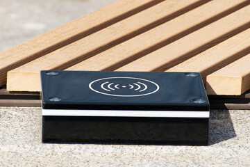a device for wireless charging of electronic gadgets is installed near a bench in a city park close-up