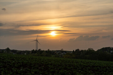 Obraz premium Two wind turbines standing next to each other in an orange-red sunset in the German countryside. Green energy concept