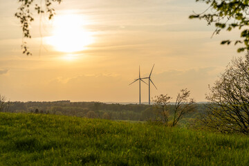 Obraz premium Two wind turbines standing next to each other in an orange-red sunset in the German countryside. Green energy concept
