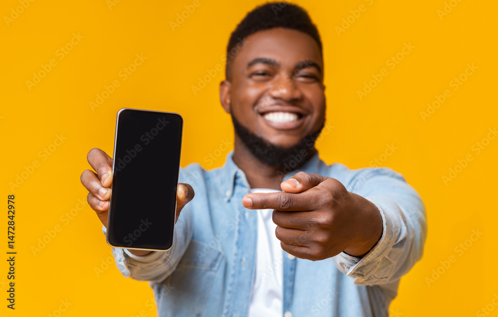 Poster check this app. cheerful afro guy holding and pointing at smartphone with black screen, yellow backg