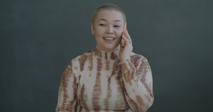 Beautiful Asian woman speaking on mobile phone smiling on black color background. Cellphone call and wireless technology concept.
