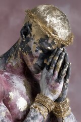 Artistic portrait of praying figure with golden crown of thorns, weathered painted skin in purple and gold tones, ornate jewelry and bracelets