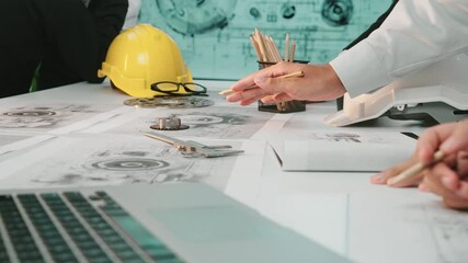 A collaborative team meeting showcases engineering designs and materials on the desk, emphasizing hands engaged in discussion, with tools and a laptop in view. SACTR