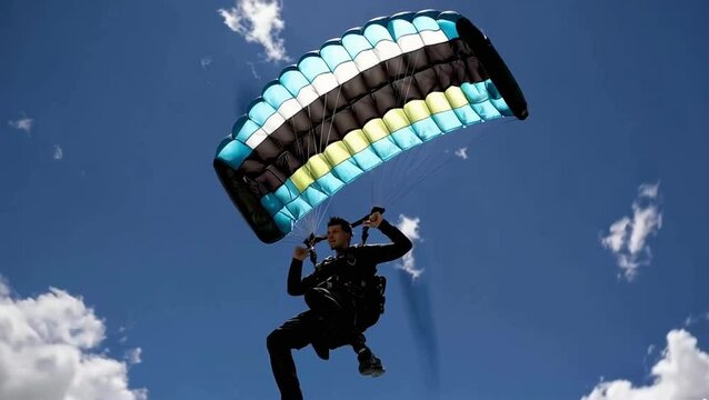Paraglider flying under a colorful canopy against a bright blue sky. Extreme sport, freedom, adventure, adrenaline and outdoor recreation concept.