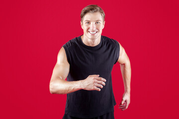 Healthy lifestyle and sports concept. Happy young sportsman running on red studio background....