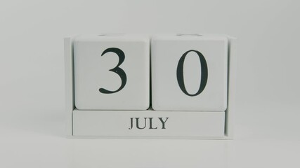  A hand flips a wooden calendar from July 30th to July 31st on a white background, highlighting the transition to the final day of the month