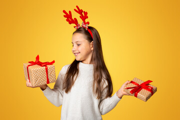 Dreams come true on Christmas. Smiling little kid girl with horns in sweater holds presents in...