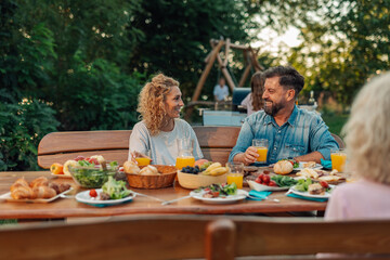 Happy family enjoying backyard barbecue, eating and drinking orange juice