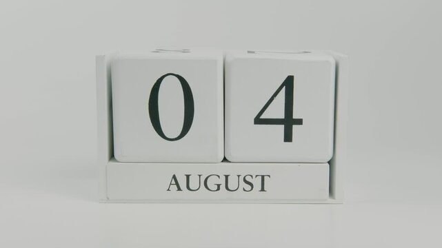 A hand flips a wooden calendar from August 4th to August 5th on a white background, indicating the passage of time