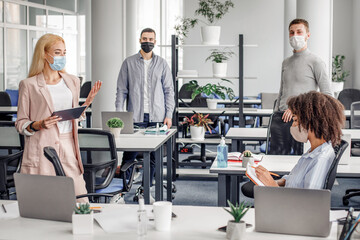 Meeting with boss. Young business woman in protective mask gives task, african american woman makes notes, guys listen to instructions in interior of modern office during COVID-19 pandemic, panorama