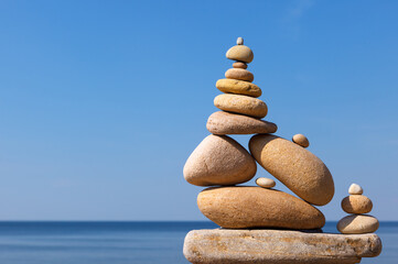 Rock zen pyramid of yellow stones on the beach against the background of the sea and blue sky....