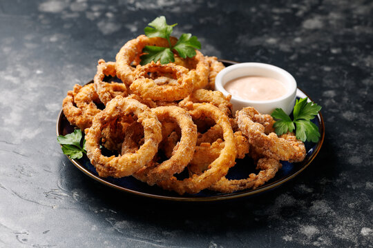 Homemade deep fried onion rings on plate with sauce.