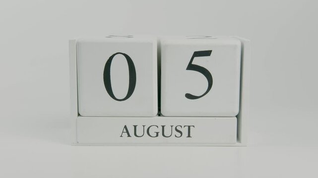 A hand flips a wooden calendar from August 5th to August 6th on a white background, symbolizing the shift to a new day