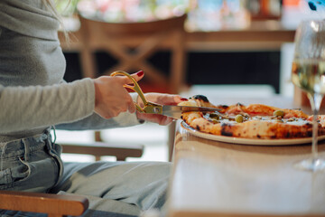 Woman cutting pizza with scissors in restaurant