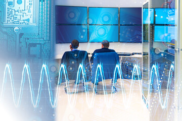 Two professionals in a control room with multiple screens and digital signal overlays, symbolizing data monitoring, cybersecurity, and network operations. – Technology. Cybersecurity.