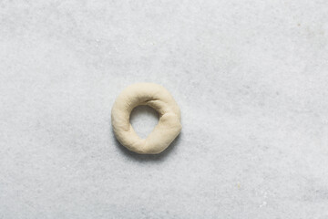 Overhead view of bagel dough being shaped on a white marble countertop, top view of shaping...