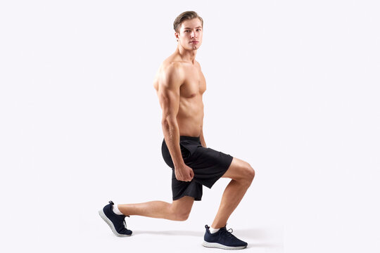 Strong young guy with sexy muscular body doing lunges, warming up before workout over light studio background. Full length portait of handsome shirtless man exercising, stretching legs
