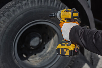 Mechanic using cordless impact wrench to tighten wheel bolts on truck tire. Concept automotive repair and maintenance work.