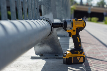 A yellow and black impact wrench stands near a metal railing at a construction site.