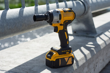 A yellow and black impact wrench stands near a metal railing at a construction site.